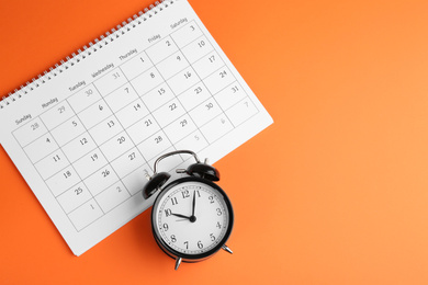 Calendar and alarm clock on orange background, flat lay. Space for text