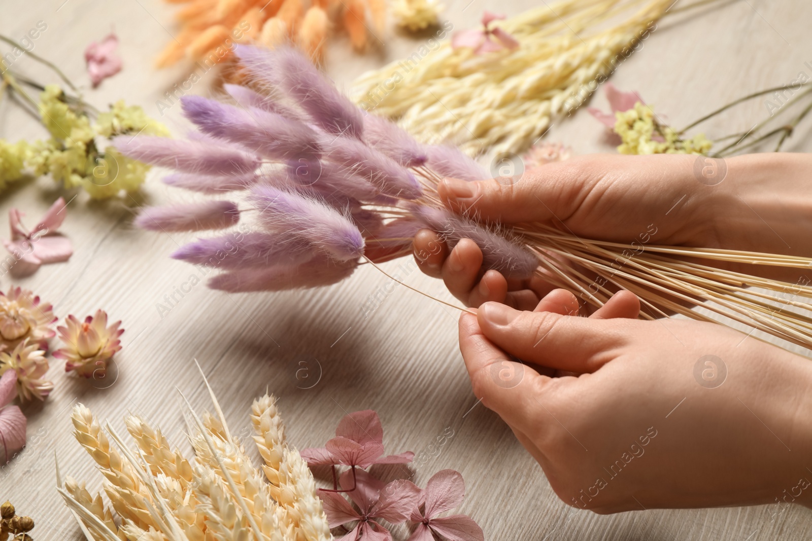 Photo of Florist making bouquet of dried flowers at white wooden table, closeup