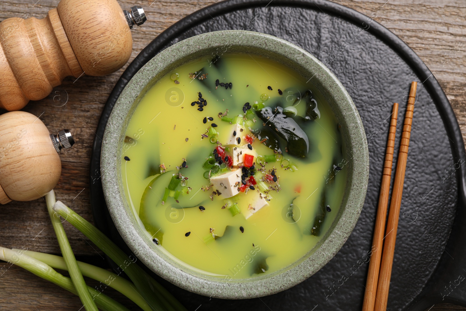 Photo of Bowl of delicious miso soup with tofu served on wooden table, flat lay