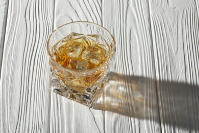 Photo of Whiskey with ice cubes in glass on white wooden table, space for text