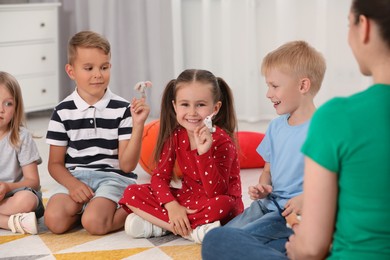 Photo of Nursery teacher and groupcute little children with finger toys for puppet show on bright rug in kindergarten. Playtime activities
