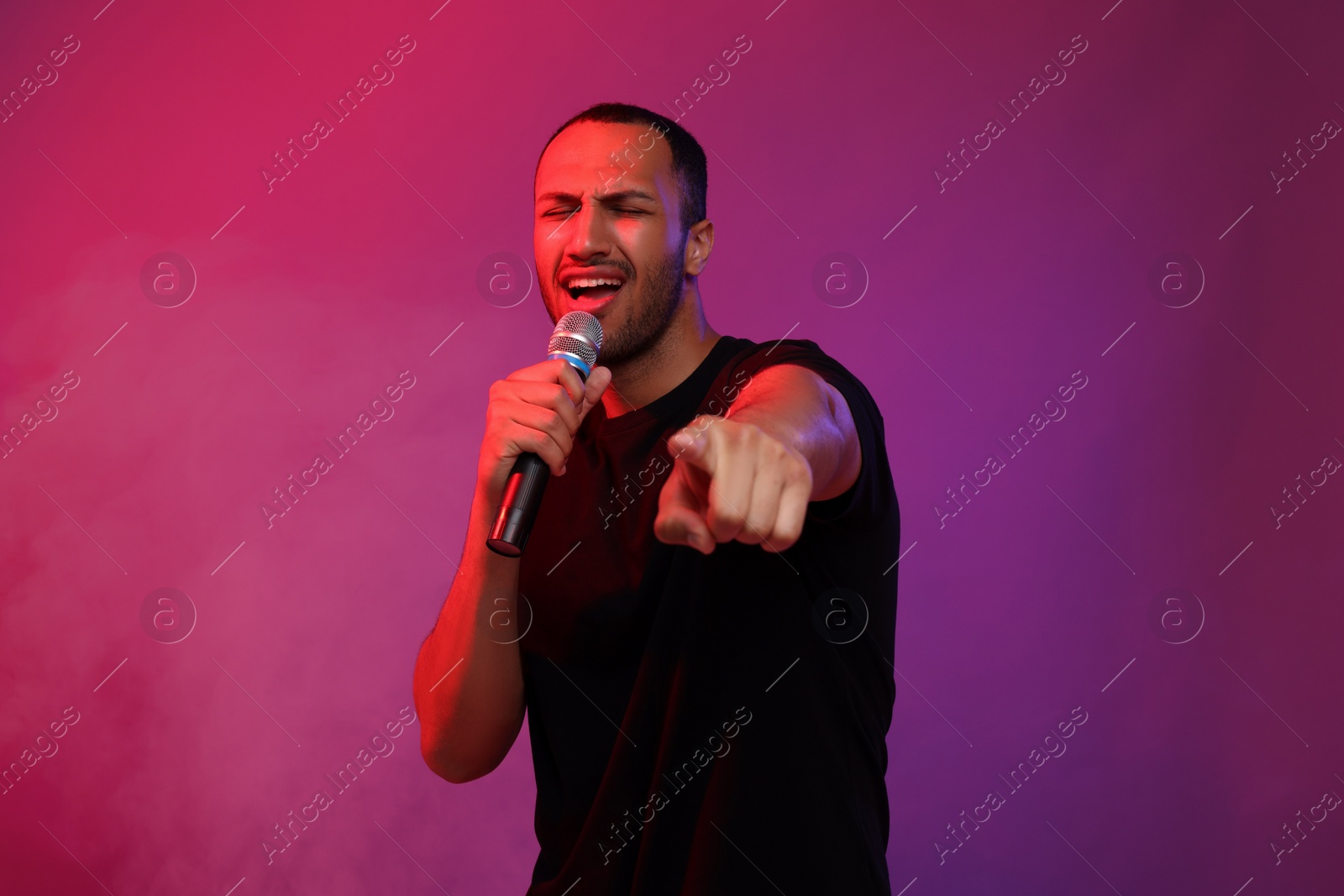 Photo of Handsome man with microphone singing on pink background. Color tone effect