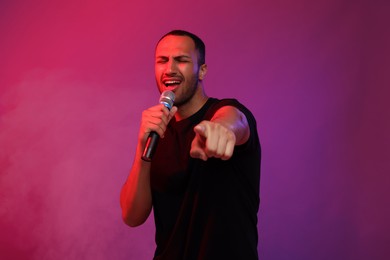 Photo of Handsome man with microphone singing on pink background. Color tone effect