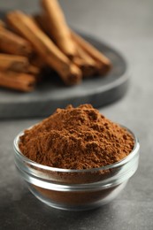 Photo of Bowl of cinnamon powder and sticks on grey table, closeup