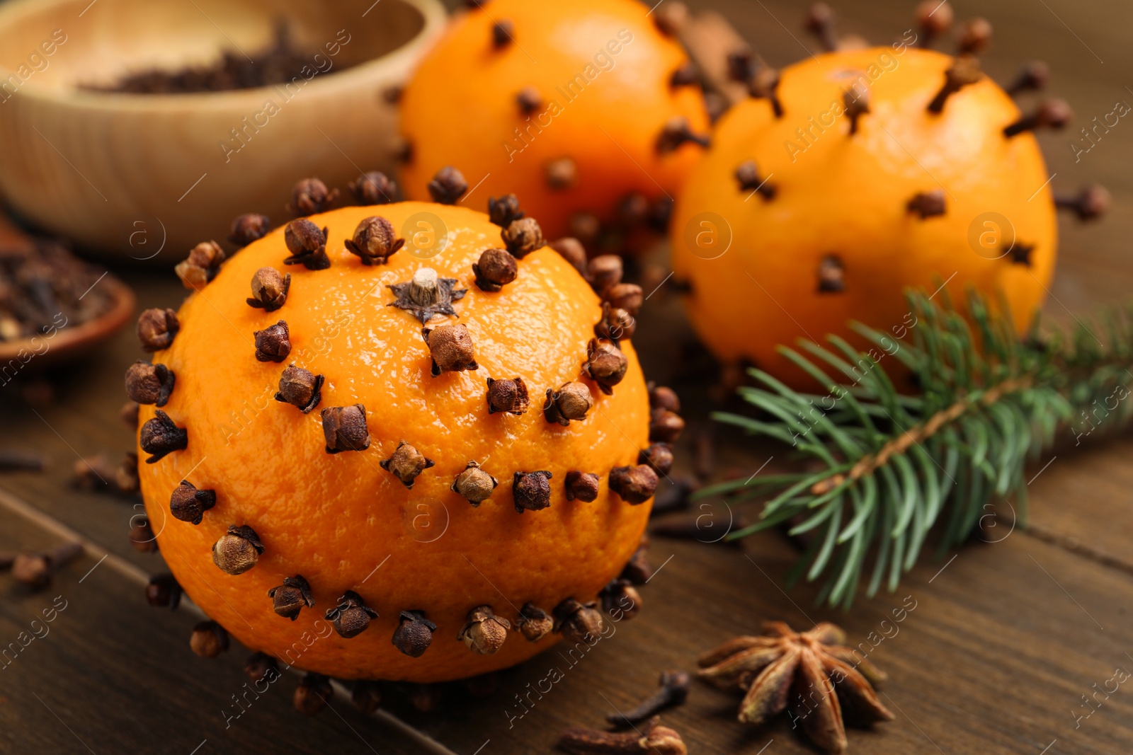 Photo of Pomander balls made of tangerines with cloves and fir branch on wooden table, closeup. Space for text