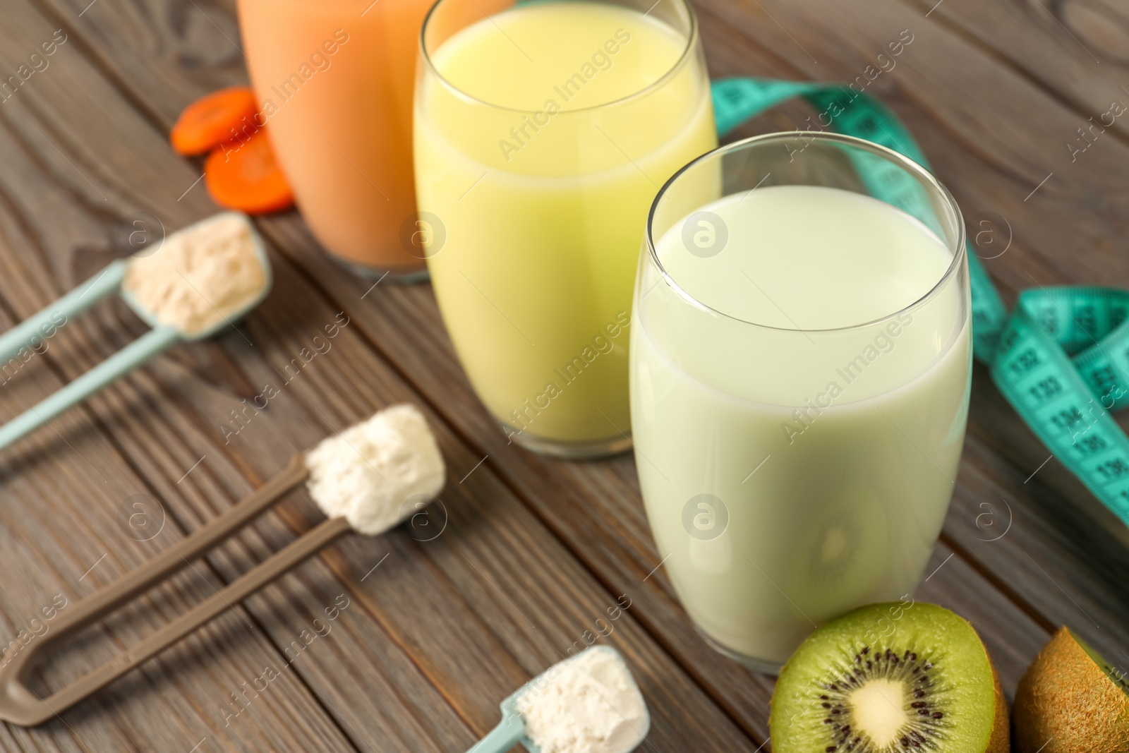 Photo of Tasty shakes, different powders, kiwi and measuring tape on wooden table, closeup. Weight loss