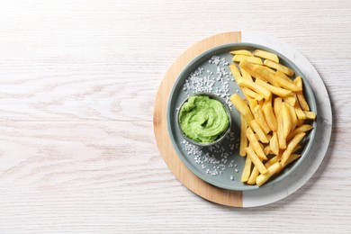 Photo of Tray with plate of french fries, salt and avocado dip on white wooden table, top view. Space for text