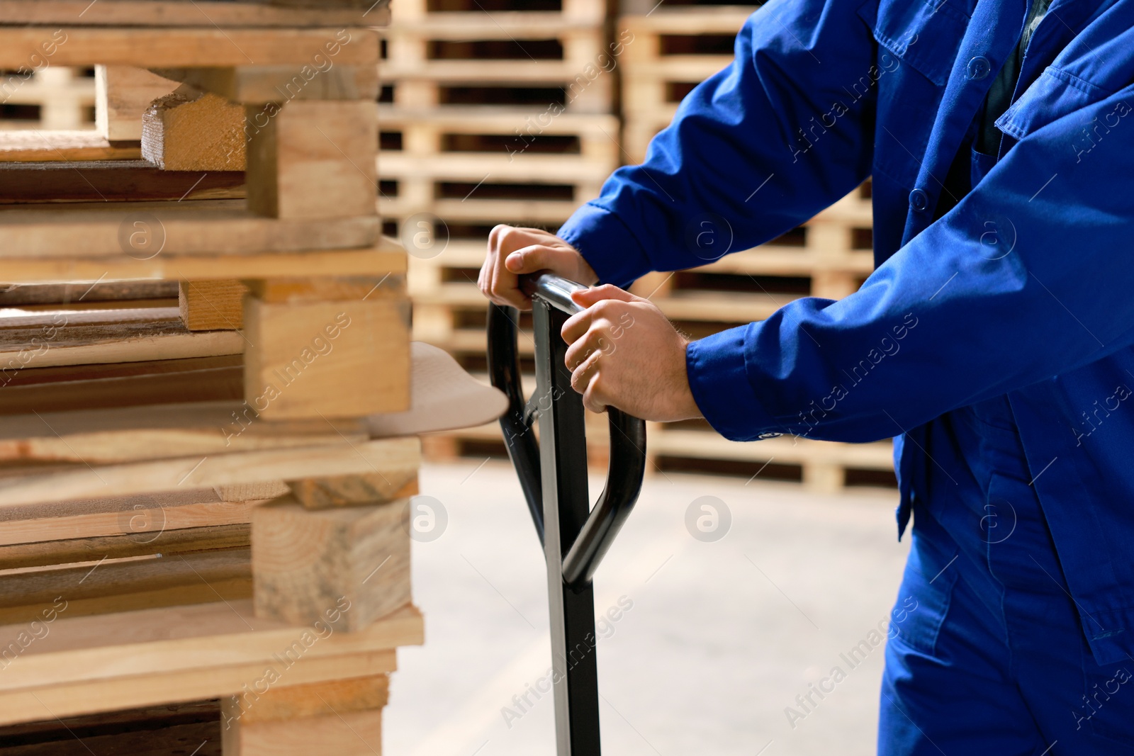 Image of Worker moving wooden pallets with manual forklift in warehouse, closeup