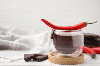 Photo of Glass of hot chocolate with chili pepper on white wooden table. Space for text