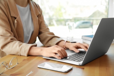 Photo of Young businesswoman using laptop at table in office, closeup