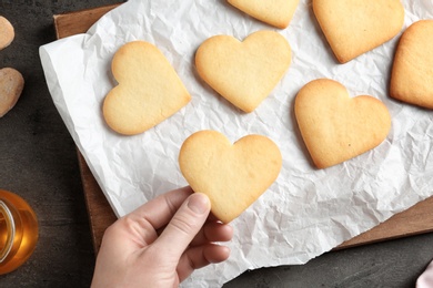 Photo of Woman holding homemade heart shaped cookie over table with pastry, top view