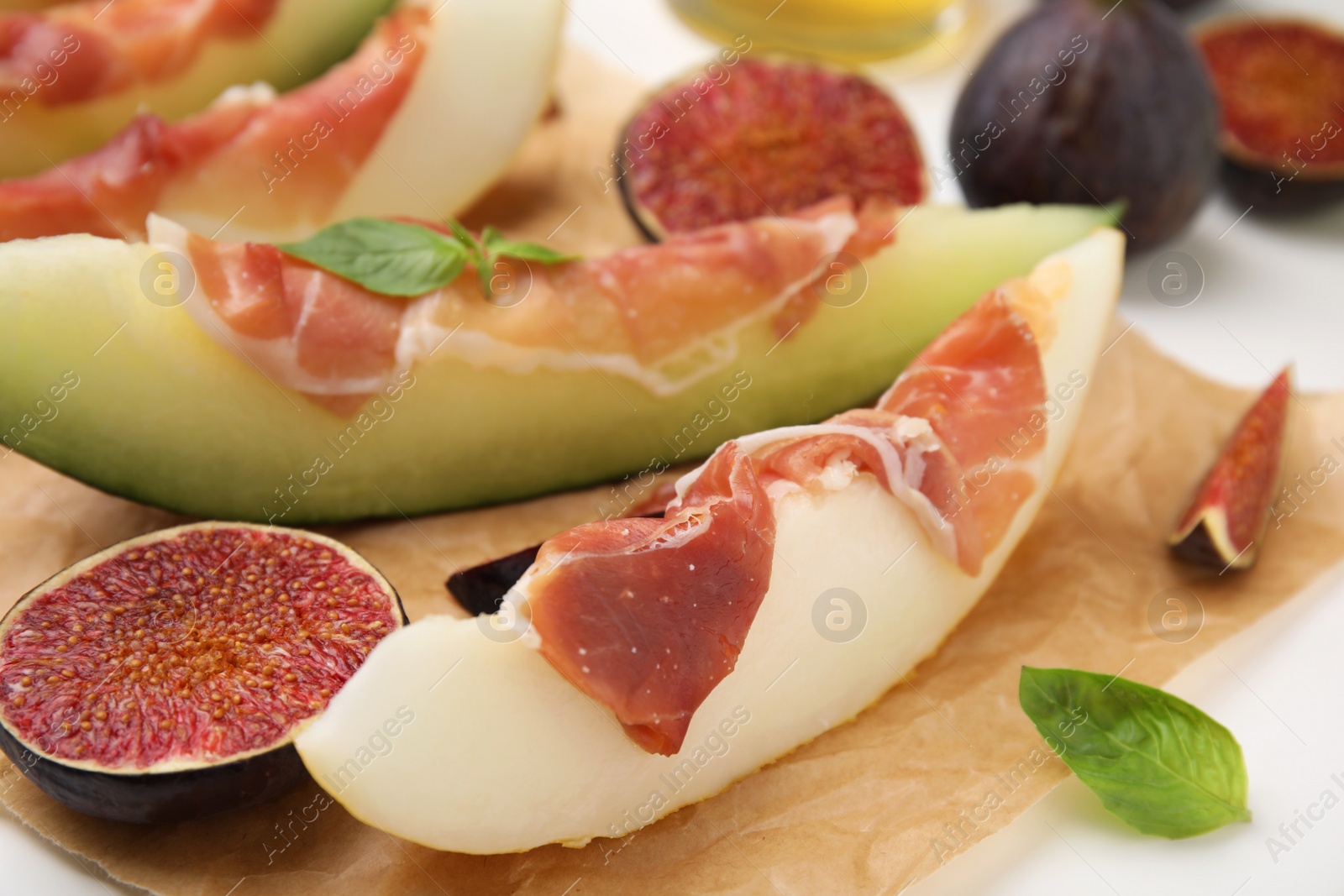 Photo of Tasty melon, jamon and figs served on parchment, closeup
