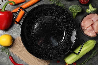 Empty iron wok surrounded by ingredients on grey table, flat lay