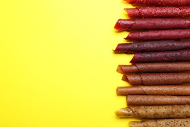 Photo of Delicious fruit leather rolls on yellow background, flat lay. Space for text