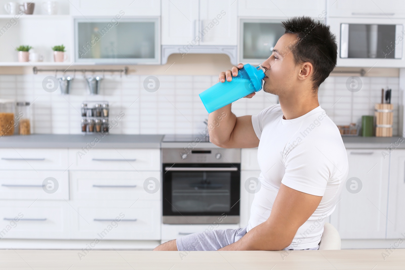 Photo of Young man drinking protein shake in kitchen. Space for text