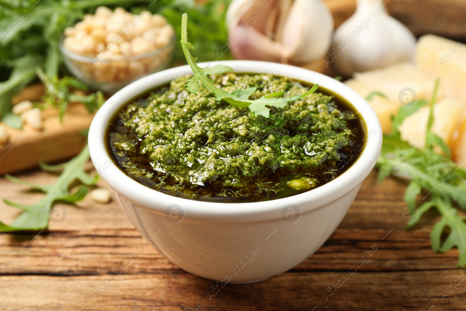 Photo of Bowl of tasty arugula pesto on wooden table, closeup