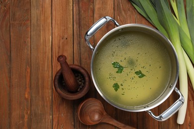 Photo of Pot with tasty bouillon, celery and peppercorn on wooden table, flat lay. Space for text