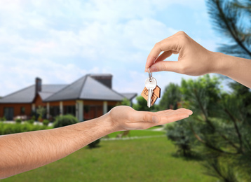Image of Real estate agent giving key to man against modern house, closeup