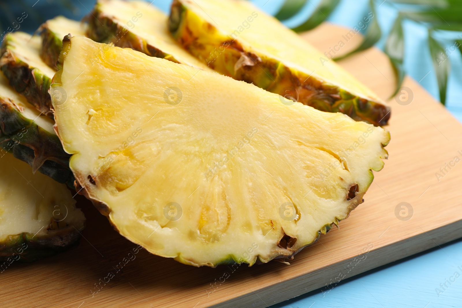 Photo of Slices of ripe juicy pineapple on light blue table, closeup