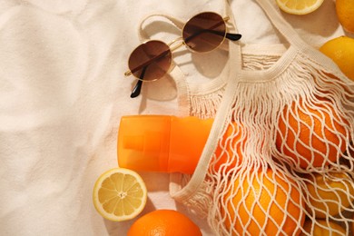 String bag with sunglasses, fruits and sunscreen on sand, flat lay. Space for text
