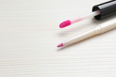 Bright lip pencil and brush of liquid lipstick on white wooden table, space for text