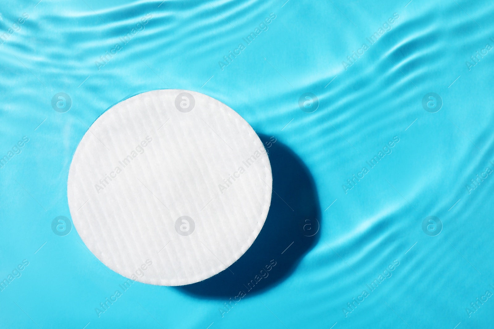 Photo of Cotton pad and micellar water on light blue background, top view. Space for text