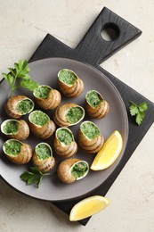 Delicious cooked snails with parsley and lemon on light table, top view