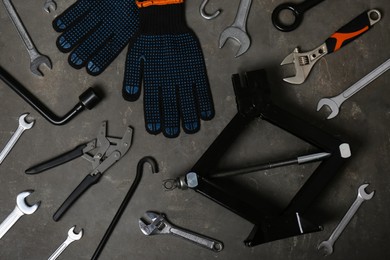 Photo of Car scissor jack, gloves and different tools on grey surface, flat lay