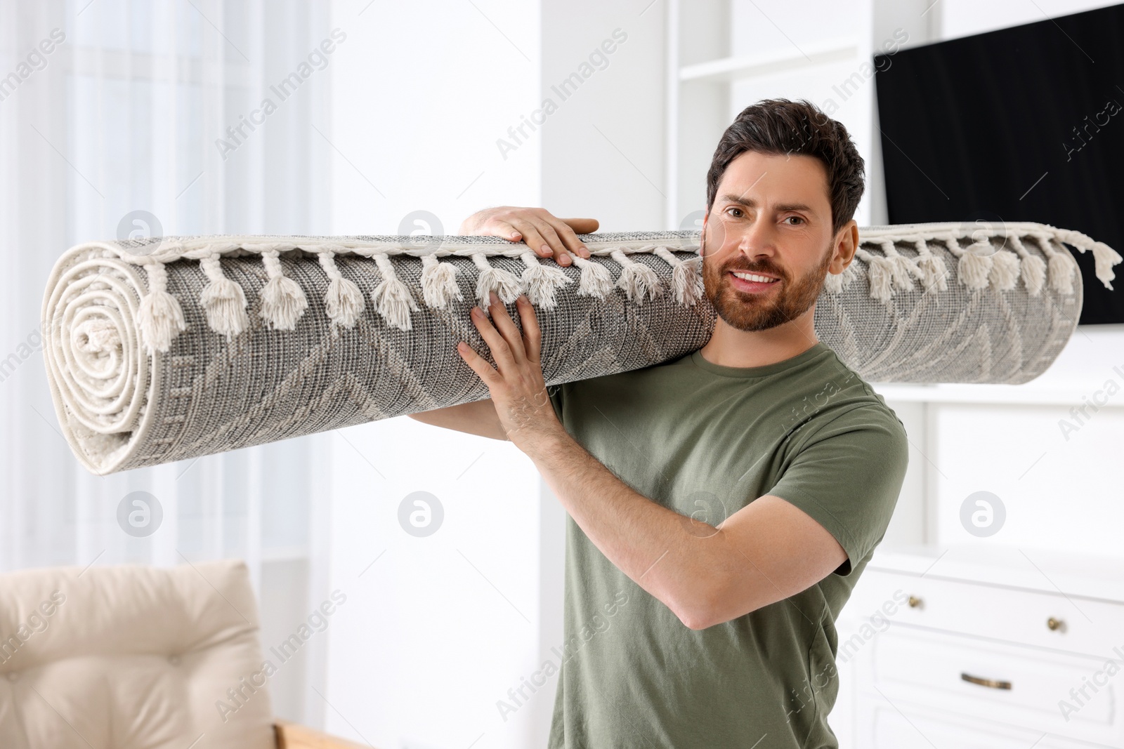 Photo of Smiling man holding rolled carpet in room