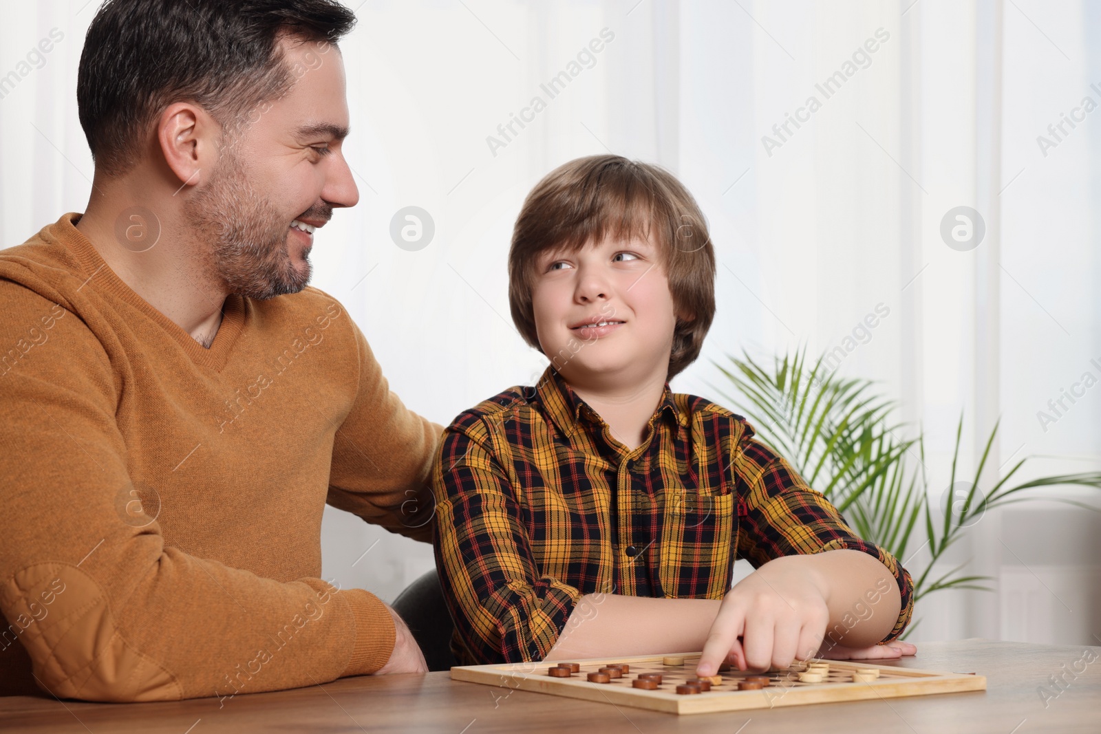 Photo of Father playing checkers with his son at table in room