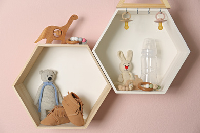 Photo of Hexagon shaped shelves with toys and child's accessories on pink wall. Interior design