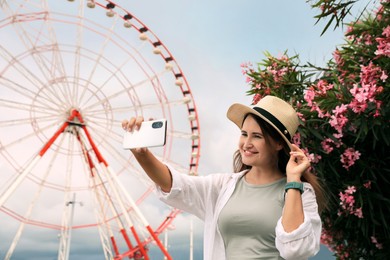 Photo of Woman taking selfie near beautiful blooming oleander and large Ferris wheel outdoors