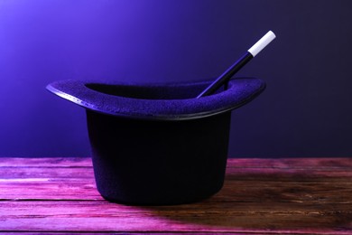 Black top hat and wand on wooden table. Magician equipment