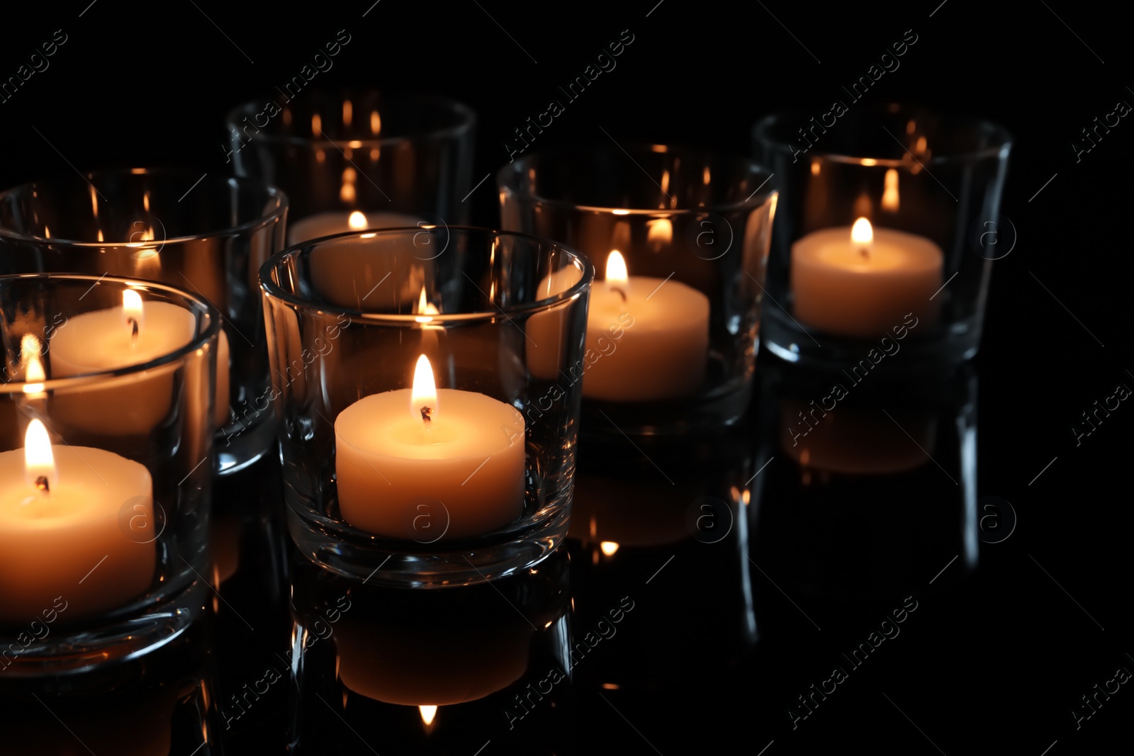 Photo of Wax candles burning on table in darkness, closeup