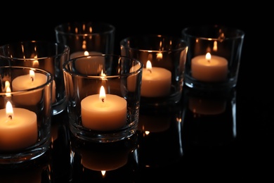 Photo of Wax candles burning on table in darkness, closeup