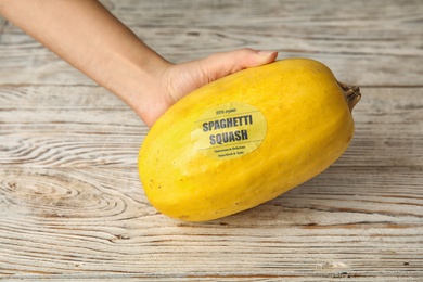 Woman holding ripe spaghetti squash on wooden table, closeup