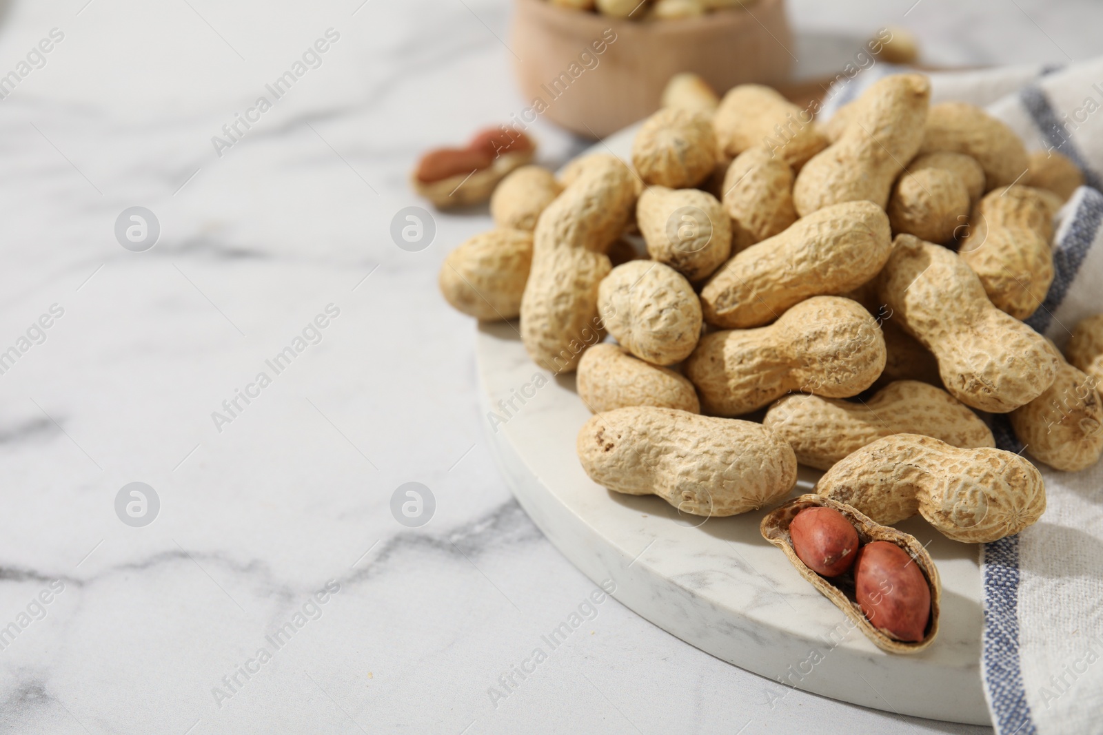 Photo of Fresh unpeeled peanuts on white marble table, closeup. Space for text