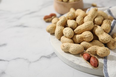 Photo of Fresh unpeeled peanuts on white marble table, closeup. Space for text