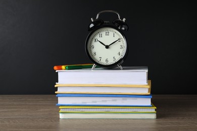 Alarm clock and stacked books on wooden table near blackboard. School time