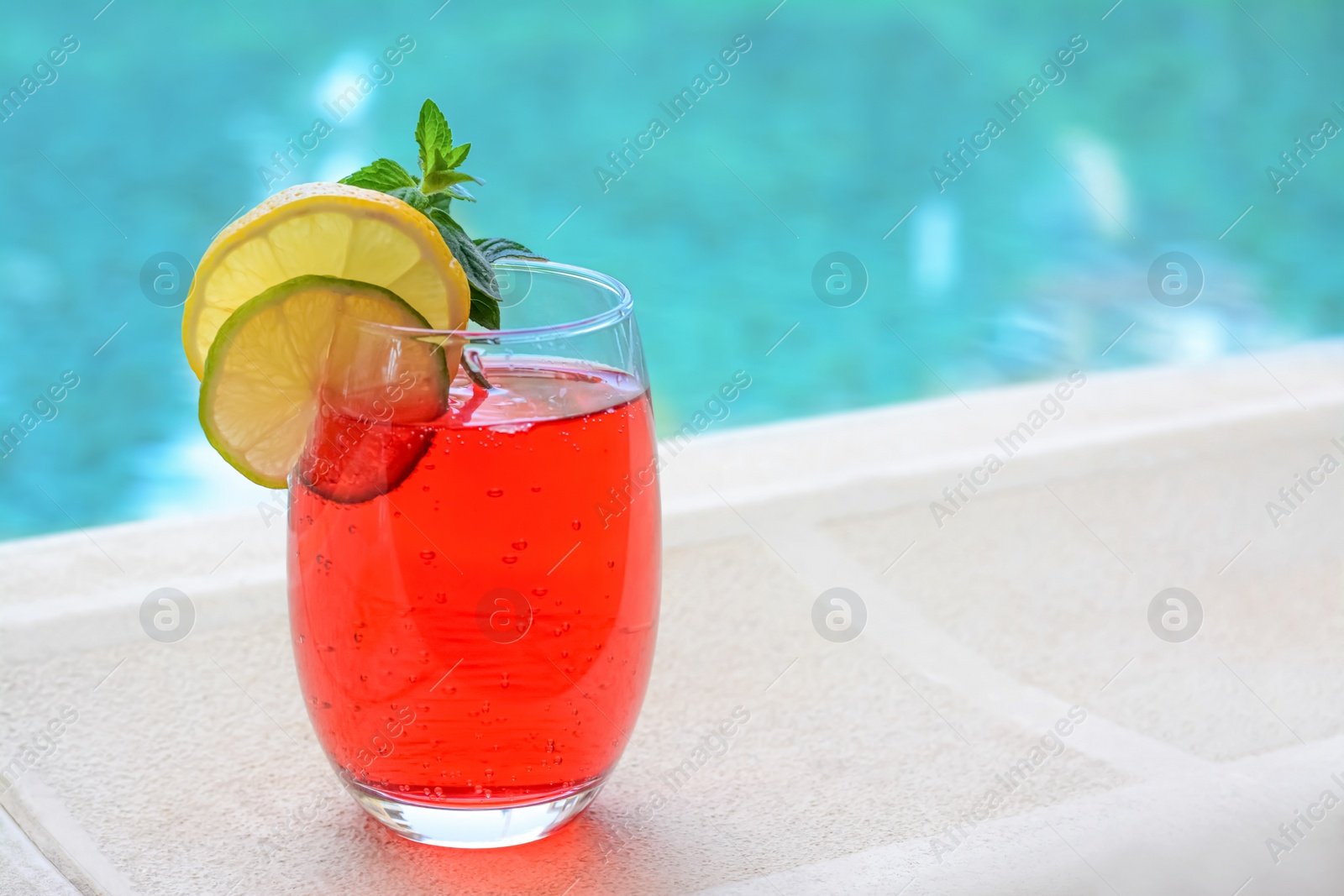 Photo of Glass of delicious cocktail near swimming pool, space for text. Refreshing drink