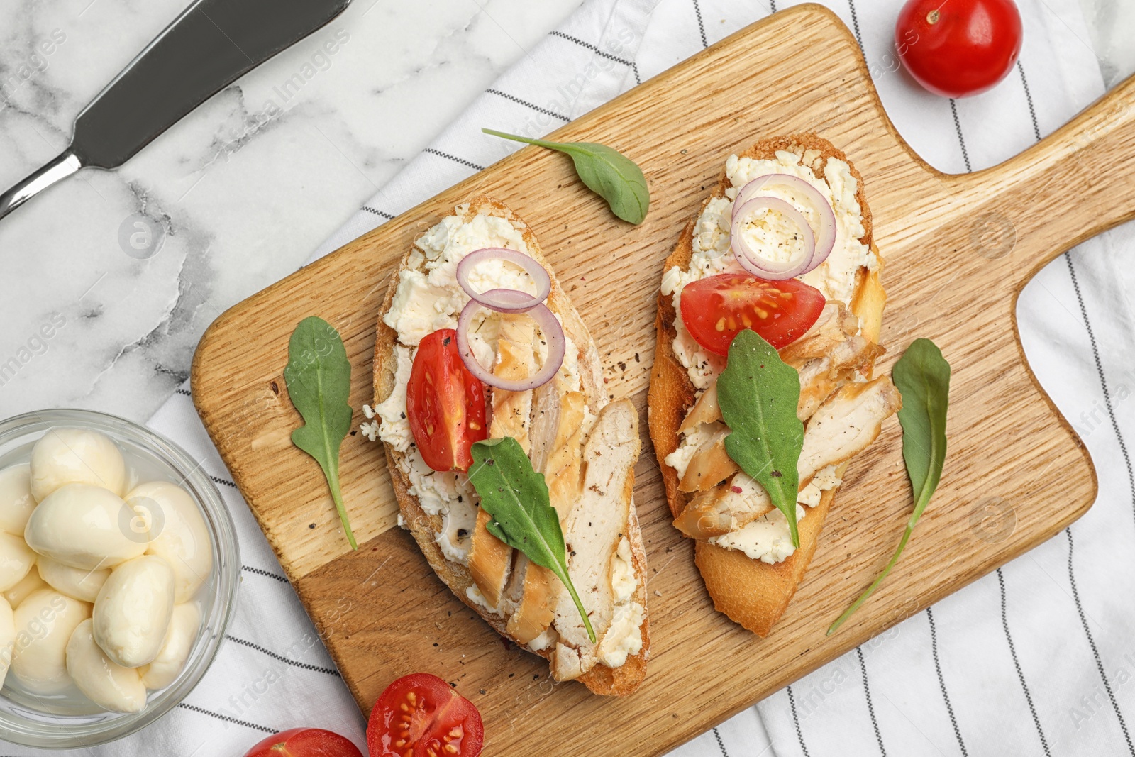 Photo of Board with delicious chicken bruschettas on white marble table, flat lay