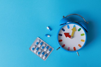 Photo of Alarm clock and pills on light blue background, flat lay. Insomnia treatment