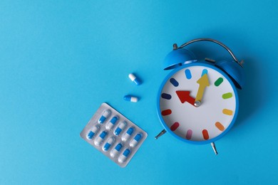 Alarm clock and pills on light blue background, flat lay. Insomnia treatment