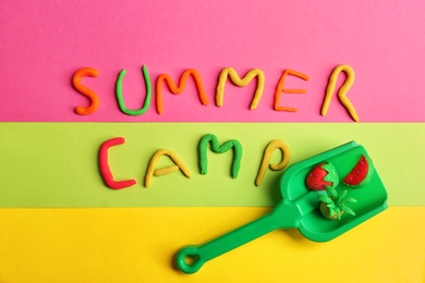 Photo of Flat lay composition with words SUMMER CAMP made from modelling clay and plastic shovel on color background