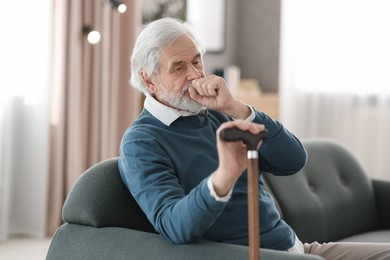 Photo of Portrait of happy grandpa with walking cane sitting on sofa indoors