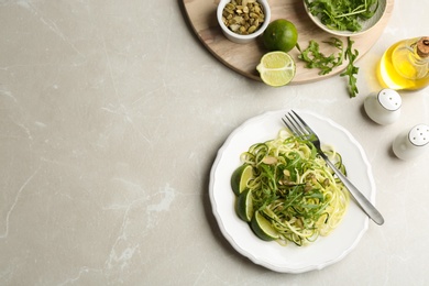 Photo of Delicious zucchini pasta with lime, pumpkin seeds and arugula served on light grey table, flat lay. Space for text