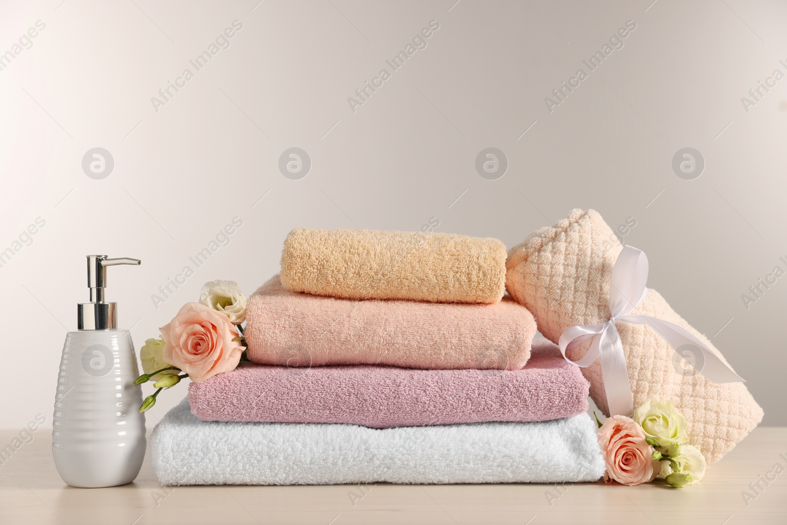 Photo of Soft towels, dispenser, roses and eustoma flowers on light wooden table