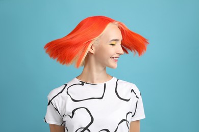 Beautiful young woman with bright dyed hair shaking head on turquoise background