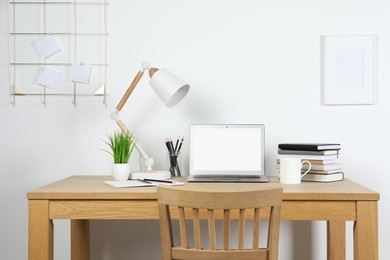 Cozy workspace with laptop, lamp and stationery on wooden desk at home