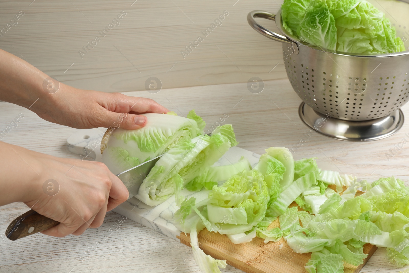 Photo of Woman cutting Chinese cabbage at white wooden kitchen table, closeup